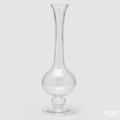 Il vaso collolungo in vetro EDG è un complemento d’arredo elegante e raffinato, caratterizzato da una silhouette slanciata che unisce leggerezza visiva e presenza scenica. La base bombata dona stabilità e morbidezza alla forma, mentre il collo lungo e affusolato crea un profilo armonioso, perfetto per valorizzare fiori singoli, rami decorativi o composizioni minimal. Il vetro trasparente con texture verticale aggiunge luminosità e un tocco di ricercatezza, rendendolo ideale per ambienti moderni e sofisticati. Caratteristiche principali Vetro trasparente di alta qualità, luminoso e resistente. Texture a righe verticali, che aggiunge eleganza e profondità visiva. Forma con base bombata e collo lungo, perfetta per composizioni verticali. Design slanciato e moderno, adatto come oggetto decorativo autonomo. Stile versatile, ideale per diversi contesti d’arredo. Materiali e finitura La lavorazione in vetro liscio e traslucido esalta i riflessi e la purezza della forma. Le righe verticali creano un effetto ottico raffinato che cattura la luce e dona movimento al vaso, rendendolo un elemento decorativo che cambia aspetto a seconda dell’illuminazione. Stile e abbinamenti Il vaso collolungo si integra facilmente in: ambienti moderni e minimalisti arredi scandinavi e naturali salotti luminosi camere dai toni neutri ingressi e consolle eleganti La trasparenza lo rende perfetto da abbinare a elementi in legno chiaro, metalli dorati, ceramiche colorate o altri vasi in vetro. Perché sceglierlo È ideale per chi desidera: un oggetto decorativo elegante e slanciato un vaso perfetto per fiori singoli o rami importanti un elemento di design che aggiunga leggerezza e luminosità un regalo raffinato e sempre apprezzato Il vaso collolungo in vetro EDG unisce design moderno, trasparenza luminosa e qualità artigianale, trasformando ogni ambiente in uno spazio più elegante, armonioso e ricercato.